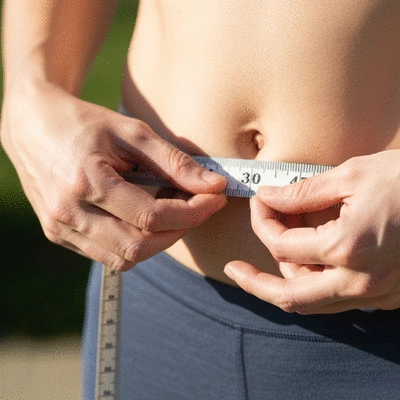 Person measuring waist circumference with a tape measure, symbolizing weight loss progress